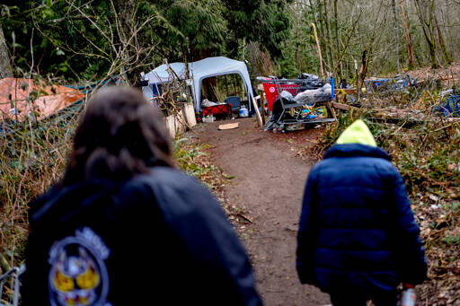Rachel Cooper, 70, who says she was introduced to fentanyl by her kids, walks back to her tent with Lummi Nation crisis outreach supervisor Evelyn Jefferson, left, at a longstanding homeless encampment near Walmart on Feb. 8 in Bellingham. The Lummi Nation declared a state of emergency due to the fentanyl crisis in 2023. State tribal leaders are urging lawmakers to pass a bill that would send at least $7.75 million in funding to tribal nations to help them stem a dramatic rise in opioid overdose deaths. (Lindsey Wasson/The Associated Press)