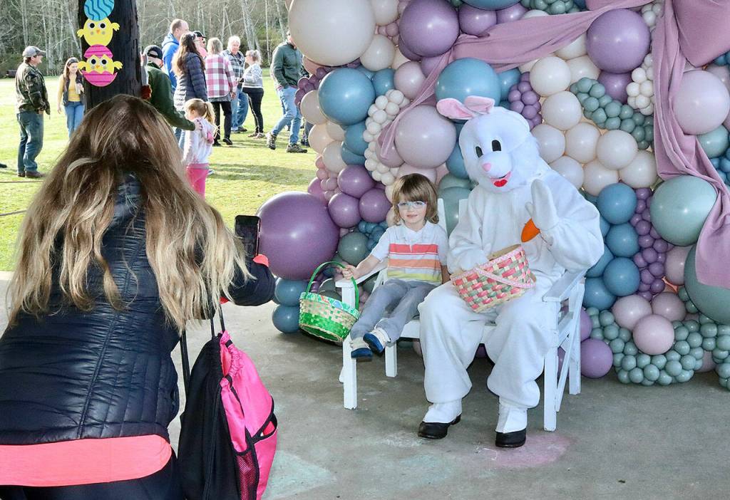 Stefano Perruccio, as the Easter Bunny, sits with Maximilian Dempsey, 5, while Holly Dempsey photographs. The 21st annual Kitchens Easter Egg Hunt was held Saturday at Crescent School in Joyce. Three divisions, for kids 3 and younger, ages 4 to 6 and 8 to 12 were on separate parts of the playground and football field. Several hundred kids and their parents filled the grounds for the hunt. (Dave Logan/for Peninsula Daily News)