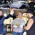 Instructor Josh Taylor, left, points out the workings of an electric vehicle on Wednesday at the Auto Technology Certification Program at Peninsula College. Nick Schommer, center, and Brian Selk get ready to do some testing on the electric autos parts from underneath the vehicle. (Dave Logan/for Peninsula Daily News)