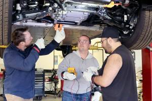Instructor Josh Taylor, left, points out the workings of an electric vehicle on Wednesday at the Auto Technology Certification Program at Peninsula College. Nick Schommer, center, and Brian Selk get ready to do some testing on the electric autos parts from underneath the vehicle. (Dave Logan/for Peninsula Daily News)