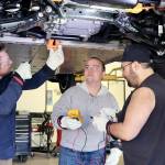 Instructor Josh Taylor, left, points out the workings of an electric vehicle on Wednesday at the Auto Technology Certification Program at Peninsula College. Nick Schommer, center, and Brian Selk get ready to do some testing on the electric autos parts from underneath the vehicle. (Dave Logan/for Peninsula Daily News)