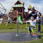 Three-year-old Archie Hanson takes a spin on a merry-go-round pushed by his mother, Justine Hanson of Port Angeles, with sister Arlene Hanson 7 months, during Sundays grand reopening of the Dream Playground at Erickson Playfield in Port Angeles. The playground was rebuilt earlier this month by volunteers after an arson fire destroyed much of the playground equipment in December. Although there are still details to attend to and minor adjustments to be made, the facility will be open daily from dawn until dusk. (KEITH THORPE/PENINSULA DAILY NEWS)