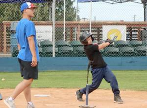 A pitch, hit and run competition was held Monday at Civic Field in Port Angeles hosted by the Port Angeles Lefties. More than 50 kids from 7 to 14 years old, some from as far away as Seattle, competed for prizes and a chance to advance to state and regional competitions. Here, Jackson Carmichael, 8, of Port Angeles takes a mighty swing off a tee as Port Angeles Leftie Kosei Suzuki assists. (Dave Logan/for Peninsula Daily News)