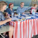 Pie contest judges, from left, Jeff Tocher, Laurel Hargis and Clallam County Commissioner Randy Johnson, along with event sponsor Country Aire Natural Foods representatives Kristina Fallon, Katie Meyers and Caeron Alarcon, make their choices during Thursdays annual Independence Day apple pie contest at Port Angeles City Pier. A total of 26 pies were entered into the contest with first-place honors going to Xaven McCarty of Seattle, Elisabeth Pennell of Mukilteo in second and Selena Reach of Port Angeles taking third. The contest was dedicated the late legacy judge and former Peninsula Daily News publisher John Brewer, represented by a photo in front of an empty chair. (Keith Thorpe/Peninsula Daily News)