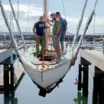 From left, Leland Gibson, Tucker Piontek and Jeff Matthews are lowered into the water aboard Fern, a Nordic folk boat commissioned by Michigan resident Charles Jahn, who was present to see his boat in the water for the first time on Friday at Port Townsends Boat Haven Marina. Fern was built over three years by three separate classes of students at The Northwest School of Wooden Boatbuilding. (Elijah Sussman/Peninsula Daily News)