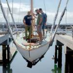 From left, Leland Gibson, Tucker Piontek and Jeff Matthews are lowered into the water aboard Fern, a Nordic folk boat commissioned by Michigan resident Charles Jahn, who was present to see his boat in the water for the first time on Friday at Port Townsends Boat Haven Marina. Fern was built over three years by three separate classes of students at The Northwest School of Wooden Boatbuilding. (Elijah Sussman/Peninsula Daily News)
