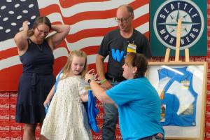 Jessica Davis helps Jordyn Mancuso-Staus put on a personalized vest during a ribbon cutting for the remodel of the Sequim Walmart as Jordyn's grandmother Donna Staus, left, and Jessica's husband John-Paul Davis watch. The Davises presented Donna with a shadowbox with her late-husband Lynie Staus' work vest. He died May 1 shortly before his 24th anniversary with the company. (Matthew Nash/Olympic Peninsula News Group)