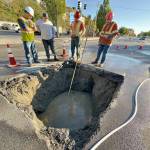 Port Townsend Public Works Director Steve King, left, discusses ways to repair the broken sewer line that developed a sinkhole late Friday night on Water Street at the entrance to the Port Townsend ferry dock, with Talon Cameron of Seaton Construction, Lane Dodson and Adam Fructas. Raw sewage continues to flow through the 70-year-old pipe and partially fills the hole. Plans were to make a temporary fix with a steel plate over the hole until more permanent repairs could be made. (Steve Mullensky/For Peninsula Daily News)