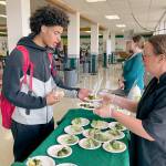Port Angeles High School junior Tucker Swain, left, tries out a sample of roasted broccoli with ranch dressing dipping sauce prepared by Stacey Larsen, the districts WSU Clallam Extension Farm to School consultant at the schools cafeteria on Friday. Including locally grown produce like the Chis Farm broccoli into meals, increasing the amount of whole grains in foods and reducing salt and added sugar are part of the school districts efforts to create healthier options and meet updated USDA nutrition standards. A new app provides students and parents a way to view menus and the nutritional content, calories and allergens in meal options. (Paula Hunt/Peninsula Daily News)