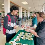 Port Angeles High School junior Tucker Swain, left, tries out a sample of roasted broccoli with ranch dressing dipping sauce prepared by Stacey Larsen, the districts WSU Clallam Extension Farm to School consultant at the schools cafeteria on Friday. Including locally grown produce like the Chis Farm broccoli into meals, increasing the amount of whole grains in foods and reducing salt and added sugar are part of the school districts efforts to create healthier options and meet updated USDA nutrition standards. A new app provides students and parents a way to view menus and the nutritional content, calories and allergens in meal options. (Paula Hunt/Peninsula Daily News)