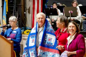 Former Marine Joseph Schwann of Port Townsend smiles as he receives a Quilt of Valor from Susan Travis, right, and another member of Quilts of Valor during the Veterans Day event at the American Legion Marvin G. Shields Memorial Post 26 in Port Townsend on Monday. Group leader Kathey Bates, left, was the emcee of the event. (Steve Mullensky/for Peninsula Daily News)