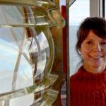 Lighthouse keeper Mel Carter next to the original 1879 Fresnel lens in the lamp room at the Point Wilson Lighthouse. (Elijah Sussman/Peninsula Daily News)