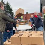 Harvey Hochstetter tosses a box of food to Cameron Needham to stack with fellow volunteers like Bill Needham, right, for the Sequim Food Banks Holiday Meal Bag Distribution event. Cameron, his father Ty and grandfather Bill were three generations helping the program. (Matthew Nash/Olympic Peninsula News Group)