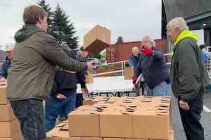 Harvey Hochstetter tosses a box of food to Cameron Needham to stack with fellow volunteers like Bill Needham, right, for the Sequim Food Banks Holiday Meal Bag Distribution event. Cameron, his father Ty and grandfather Bill were three generations helping the program. (Matthew Nash/Olympic Peninsula News Group)