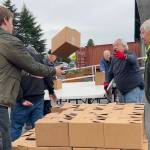 Harvey Hochstetter tosses a box of food to Cameron Needham to stack with fellow volunteers like Bill Needham, right, for the Sequim Food Banks Holiday Meal Bag Distribution event. Cameron, his father Ty and grandfather Bill were three generations helping the program. (Matthew Nash/Olympic Peninsula News Group)