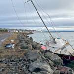 A cyclist rides by the 26-foot sloop that was dashed against the rocks along the Larry Scott Trail on Wednesday due to 30 mph winds from an atmospheric river storm buffeting the North Olympic Peninsula. A 29-year-old Port Townsend man, who was not identified, and his dog were rescued by a Coast Guard rescue swimmer from Coast Guard Air Station Port Angeles. (Steve Mullensky/for Peninsula Daily News)