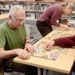 Tim Branham, left, his wife Mickey and Bill Pearl work on a 500-piece jigsaw puzzle entitled “Days to Remember.” The North Olympic Library at its main branch on South Peabody Street in Port Angeles sponsored a jigsaw puzzle contest on Saturday, and 15 contestants challenged their skills. With teams of two to four, contestants try to put together a puzzle in a two-hour time limit. Justin Senter and Rachel Cook finished their puzzle in 54 minutes to win the event. The record from past years is less than 40 minutes. The next puzzle contest will be at 10 a.m. Feb. 8. (Dave Logan/for Peninsula Daily News)