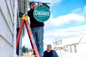 Connor Cunningham of Port Townsend, an employee of the Port of Port Townsend, hangs a sign for new business owner Lori Hanemann of Port Townsend on Friday at her shop in what was a former moorage office at Point Hudson Marina. (Steve Mullensky/for Peninsula Daily News)
