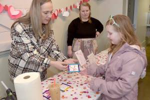Madison Canterbury, 7, of Shelton looks at a Valentines gift she created with the assistance of volunteers Chandra McGuff, left, and Nicole Lemon at a craft table set up outside the Silver Lining Cafe at The Wharf on Saturday on the Port Angeles waterfront. Youngsters were given the opportunity to create gifts and Valentines cookies during the event. (Keith Thorpe/Peninsula Daily News)