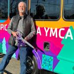Mike Speer of Bonney Lake stands with the new bus his sister Sherry Nagels estate helped pay for at the YMCA of Sequim. A quilt square with a dedication to Nagel is on the side of the bus. (Matthew Nash/Olympic Peninsula News Group)