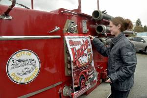 Samantha Herik, an EMT with the Port Angeles Fire Department, attaches a poster to the side of her departments vintage 1956 Seagrave fire truck during a fundraising drive on Saturday in the Swains General Store parking lot in Port Angeles. PAFD is collecting donations to rebuild the retired vehicle, known as No. 5, with a restored engine and transmission. The truck is used primarily for the annual Operation Candy Cane food bank fundraising drive, along with other promotional purposes. (Keith Thorpe/Peninsula Daily News)