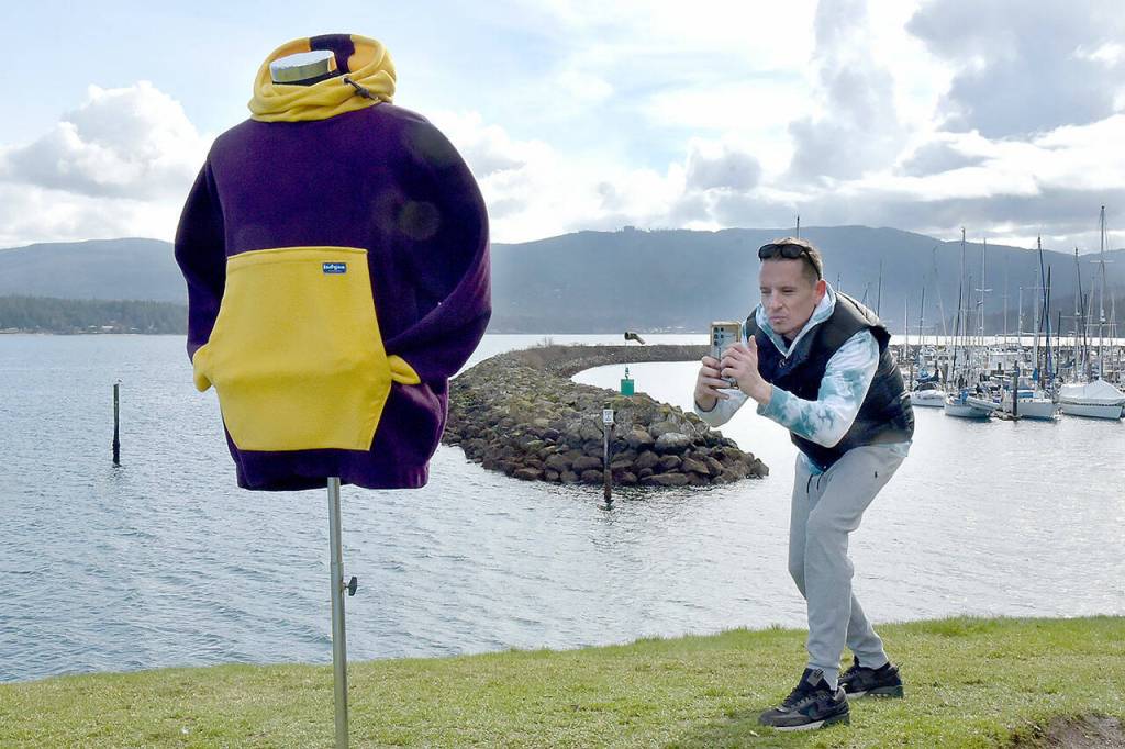 Joseph Prince takes a photo of a hoodie jacket on Wednesday on a small hill overlooking the entrance to John Wayne Marina near Sequim. Prince, a member of the Jamestown SKlallam Tribe, said the weather was ideal for adding items to the catalog of his online vintage clothing business. (Keith Thorpe/Peninsula Daily News)