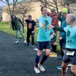Chris Hartman of the Sub Alpine Tees Team hands off the crocheted yellow banana slug baton to teammate Jon Cummings. Fellow teammates cheer on the runners at the Port Angeles Yacht Club Club exchange station Saturday. (Dave Logan/for Peninsula Daily News)