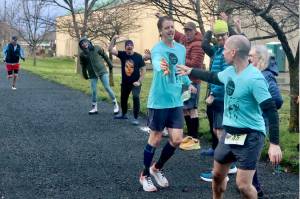 Chris Hartman of the Sub Alpine Tees Team hands off the crocheted yellow banana slug baton to teammate Jon Cummings. Fellow teammates cheer on the runners at the Port Angeles Yacht Club Club exchange station Saturday. (Dave Logan/for Peninsula Daily News)