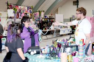 Caro Tchannie and her daughter Lola Hatch, 9, of Tulallip try a long string of beads at Squatchcon on Thursday at the Vern Burton Community Center gym in Port Angeles. Kevin VanDinter of Port Angeles was one of 60 vendors at the four day event, which continues through Sunday. (Dave Logan/for Peninsula Daily News)