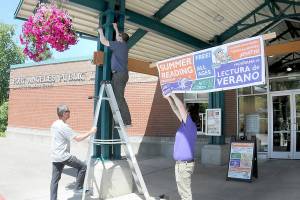 Maintenance workers, from left, Brian Phillips, Jeff Clark and Noah Mohmand, suspend a banner outside the Port Angeles Public Library to gather interest in the library systems Summer Reading Program, which runs from Friday through Aug. 23. The program offers free books and prizes for avid readers at the systems branches in Port Angeles, Sequim, Forks and Clallam Bay. (Keith Thorpe/Peninsula Daily News)