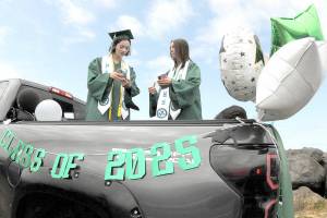Port Angeles High School twin graduates Kaylie Mast, left, and Kendall Mast, communicate with their friends by text while waiting for the start of the 2025 graduation parade on Friday. The parade began at Ediz Hook and culminated with a formal ceremony Friday evening at Port Angeles Civic Field. (Keith Thorpe/Peninsula Daily News)