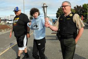 Special Olympian Deni Isett, center, holds a ceremonial torch with Clallam County Sheriff Brian King, right, accompanied by Lt. Jim Thompson of the Lower Elwha Klallam Tribal Police on a leg of the Law Enforcement Torch Run on the Olympic Discovery Trail at Port Angeles City Pier. Tuesdays segment of the run, conducted mostly by area law enforcement agencies, was organized to support Special Olympics Washington and was to culminate with a community celebration at 7 Cedars Casino in Blyn. (Keith Thorpe/Peninsula Daily News)