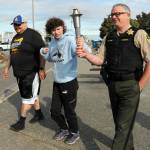 Special Olympian Deni Isett, center, holds a ceremonial torch with Clallam County Sheriff Brian King, right, accompanied by Lt. Jim Thompson of the Lower Elwha Klallam Tribal Police on a leg of the Law Enforcement Torch Run on the Olympic Discovery Trail at Port Angeles City Pier. Tuesdays segment of the run, conducted mostly by area law enforcement agencies, was organized to support Special Olympics Washington and was to culminate with a community celebration at 7 Cedars Casino in Blyn. (Keith Thorpe/Peninsula Daily News)