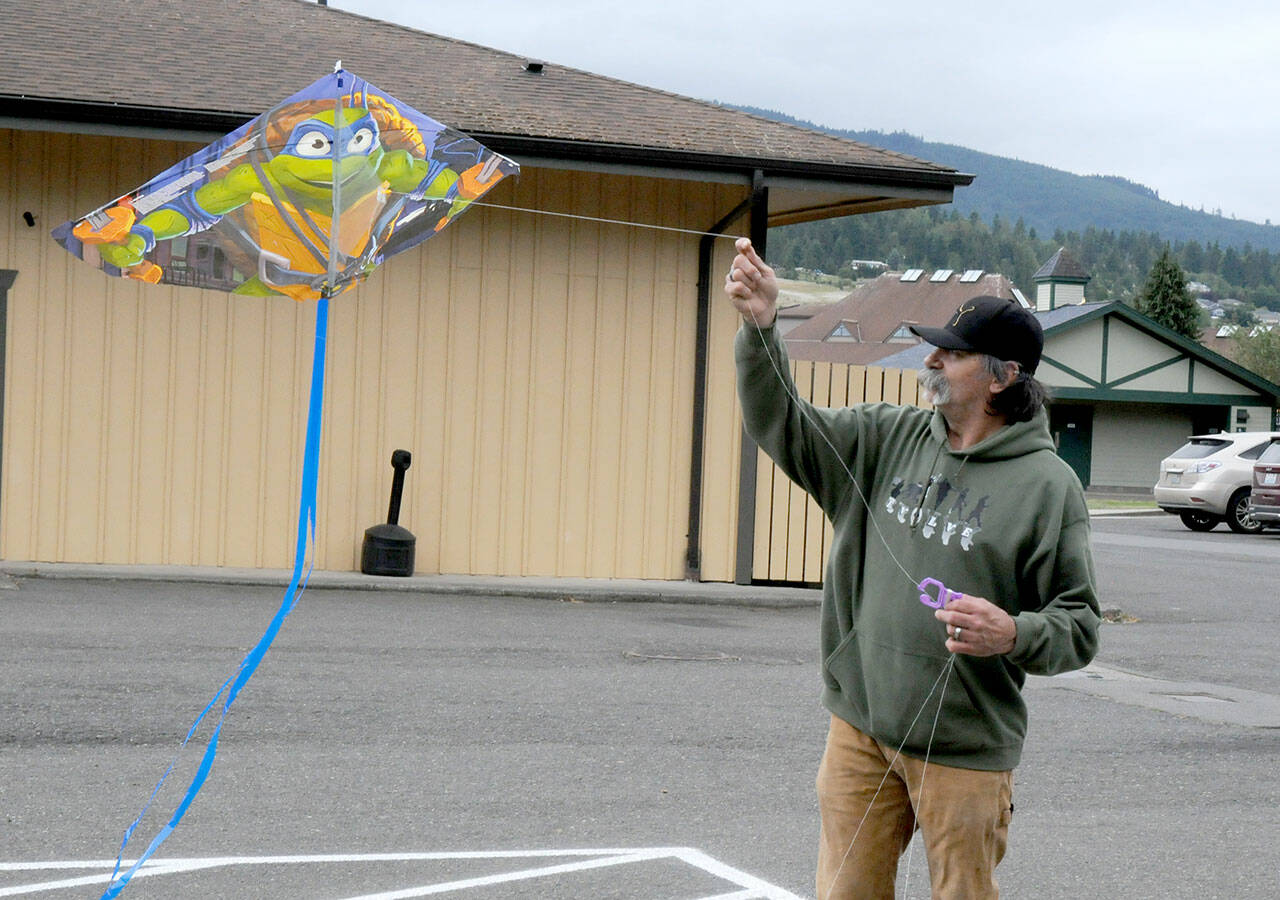 Randy Nobbs of Sequim attempts to get a kite to take flight on Wednesday at Carrie Blake Park in Sequim. A line of sheltering trees made it difficult to launch the kite until he received help from family members to get the aerial glider above the tree line and into the breeze. (Keith Thorpe/Peninsula Daily News)