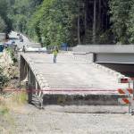 KEITH THORPE/PENINSULA DAILY NEWS
Construction workers stand on what remains of the old U.S. 101 bridge over the Elwha River on Wednesday as the aging structure is dismantled. The old bridge, built in 1926, was in danger of washout when the river beneath changed course and engineers discovered the bridge piers were built on gravel instead of bedrock, leading to constructon of a new bridge, at right, which was opened to traffic in 2024. The old bridge was to remain in place until a fish-spawning window, which runs from mid-July until the end of August.