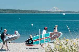 Beachgoers look for a spot on the sand on Sunday afternoon at Fort Worden State Park in Port Townsend. Mount Rainier looms in the distance. (Steve Mullensky/for Peninsula Daily News)