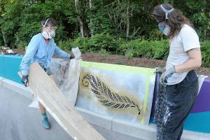 Artists Heather Sparks, left, and Zeo Boekbinder set up a stencil of a fern leaf in an effort to decorate an otherwise-drab concrete roadside divider along Race Street south of Lauridsen Boulevard on Wednesday in Port Angeles. The divider work was part of a larger project to beautify the Race Street corridor from Eighth Street to Hurricane Ridge Road, which included improved traffic lanes, pedestrian and bicycle lanes and decorative lighting. Long-term plans call for similar improvements to Race Street, extending to First and Front streets. (Keith Thorpe/Peninsula Daily News)