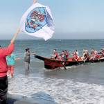 Tribal member Jerry Foster waves a Lower Elwha Klallam tribal flag as a canoe paddled by members of the Port Gamble SKlallam Tribe arrives at Elwha Beach at Angeles Point on Thursday. (Keith Thorpe/Peninsula Daily News)