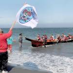 Tribal member Jerry Foster waves a Lower Elwha Klallam tribal flag as a canoe paddled by members of the Port Gamble SKlallam Tribe arrives at Elwha Beach at Angeles Point on Thursday. (Keith Thorpe/Peninsula Daily News)