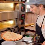 Flutter By Pizza Pie owner and operator Mark Ennis pulls a cheese pizza from the oven. (Elijah Sussman/Peninsula Daily News)