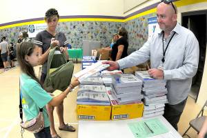 Amelia Solomon, 9, a fourth-grade student at Jefferson Elementary, receives a package of notebook paper from Nick Carlson of Olympic Medical Center as Amelias mother, Hermina Solomon, accompanies her during the Port Angeles School District Back to School Fair on Saturday at Jefferson. The event offered school supplies to students, as well as health information, family services and a picnic meal. (Keith Thorpe/Peninsula Daily News)
