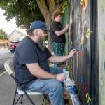 Jesse Adams, front, of Port Townsend, and son Evan of Allyn paint eyes on a section of the fence surrounding Port Townsends Memorial Field as their contribution to the Outsiders Street Art Project Port Townsend during Jefferson Countys first community public art project. Adams project, titled Eye Strain, had to be submitted for approval before work could begin. Each artist had an 8-foot section of fence to work on. The fence will be taken down, most likely next spring, to be replaced with a new one. (Steve Mullensky/for Peninsula Daily News)