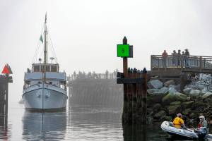 From out of the fog in Port Townsend Bay on Thursday morning, the 97-year-old yacht Blue Peter passes by spectators who lined the pier at the entrance to Point Hudson Marina. Harbormasters, lower right, are ready to guide the 96-foot vessel to its place at the dock in preparation of the opening of the 47th Wooden Boat Festival, which opens today. The festival will run until Sunday afternoon. (Steve Mullensky/for Peninsula Daily News)