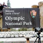 Lorena Miramontes Morley, left, and her spouse, Mandy Miramontes Morley, both of Anaheim, Calif., use a remote-controlled camera to take a self-portrait on the Olympic National Park entrance sign on Tuesday in Port Angeles. (Keith Thorpe/Peninsula Daily News)