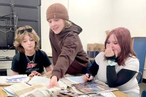 Stevens Middle School eighth-grader Linda Venuti, left, and seventh-graders Noah Larsen and Airabella Rogers pour through the contents of a time capsule found in August by electrical contractors working on the new school scheduled to open in 2028. The time capsule was buried by sixth graders in 1989. (Paula Hunt/Peninsula Daily News)