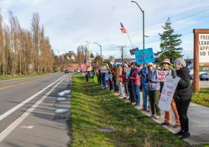Members of Port Townsend Indivisible, a political protest group, begin to amass along Sims Way on Saturday in the first rally of 2026. The group was called to action in protest of the U.S. government and Donald Trump ousting the president of Venezuela overnight. Gina McMather, second from the right, a member of the Indivisible leadership team, led the pop-up rally. (Steve Mullensky/for Peninsula Daily News)