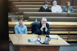 Cole Douglas, who was sentenced Thursday after he pleaded guilty to the March 2025 hit and run that seriously injured Sequim middle-schooler Colton Dufour, listens to Judge Elizabeth Stanley as Coltons mother, Cherie Tachell, seated several rows back, smiles at her son just minutes before Douglas was taken into custody to begin serving a 12-month jail sentence. Seated beside them is victims advocate Molly Ramsey, who works in the Clallam County prosecuting attorneys office and read a victims impact statement to the court during hearing. (Clallam County Superior Court)