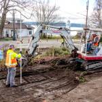 Workers from Van Ness Construction in Port Hadlock, one holding a grade rod with a laser pointer, left, and another driving the backhoe, scrape dirt for a new sidewalk of civic improvements at Walker and Washington streets in Port Townsend on Thursday. The sidewalks will be poured in early February and extend down the hill on Washington Street and along Walker Street next to the pickle ball courts. (Steve Mullensky/for Peninsula Daily News)