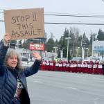 Wendy Rae Johnson waves to cars on the north side of U.S. Highway 101 in Port Angeles on Saturday during a demonstration against U.S. Immigration and Customs Enforcement operations in Minnesota. On the other side of the highway is the Peninsula Handmaids in red robes and hoods. (Dave Logan/for Peninsula Daily News)