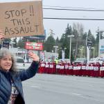 Wendy Rae Johnson waves to cars on the north side of U.S. Highway 101 in Port Angeles on Saturday during a demonstration against U.S. Immigration and Customs Enforcement operations in Minnesota. On the other side of the highway is the Peninsula Handmaids in red robes and hoods. (Dave Logan/for Peninsula Daily News)